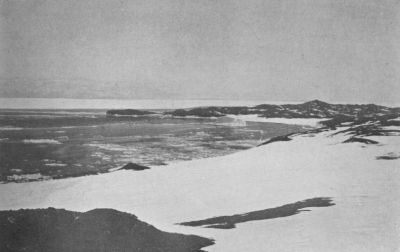 A photograph of Cape Royds. Snow ends at the sea, which has ice floating on it.