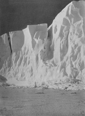 A photograph of a high vertical cliff face made of ice, meeting a field of ice below.