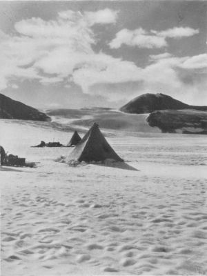 A photograph of two pyramidal tents amidst snowy hills.