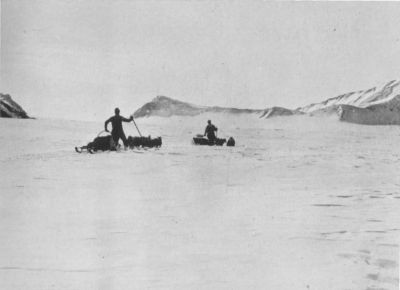 A photograph of two men in sleds with a team of dogs.
