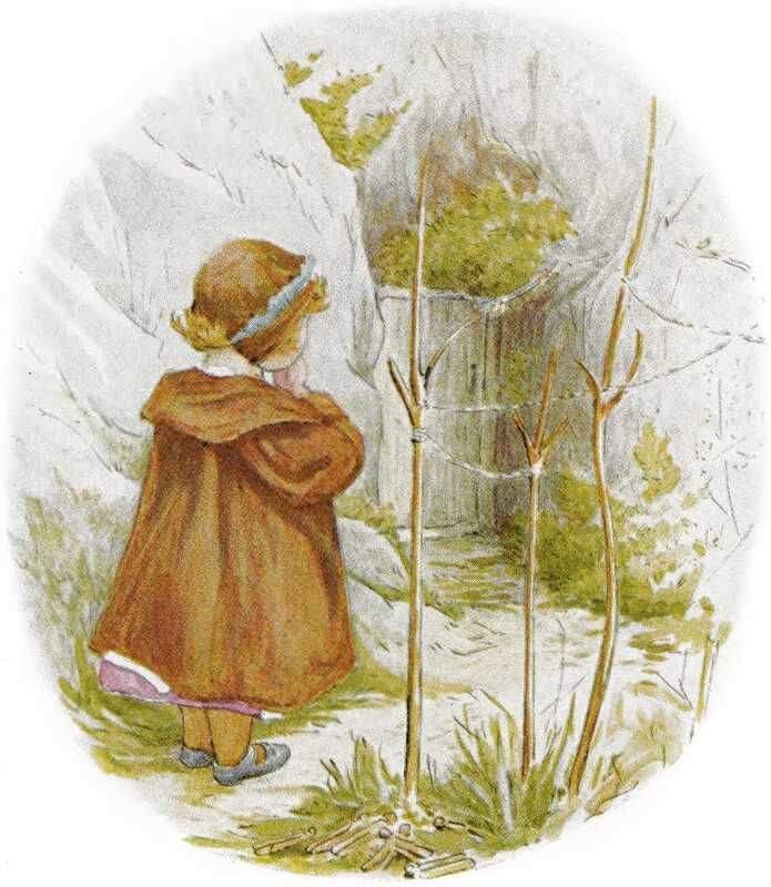 Lucie has her hands to her mouth as she looks at a small grey door built into a rock. String is tied between some small bare trees next to her.