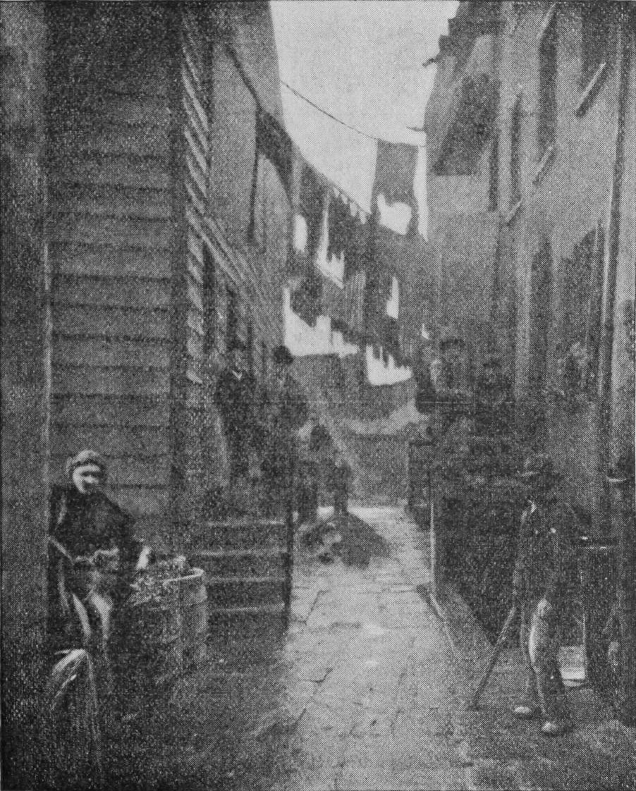 Several people stand in an alley between houses and look towards the camera.