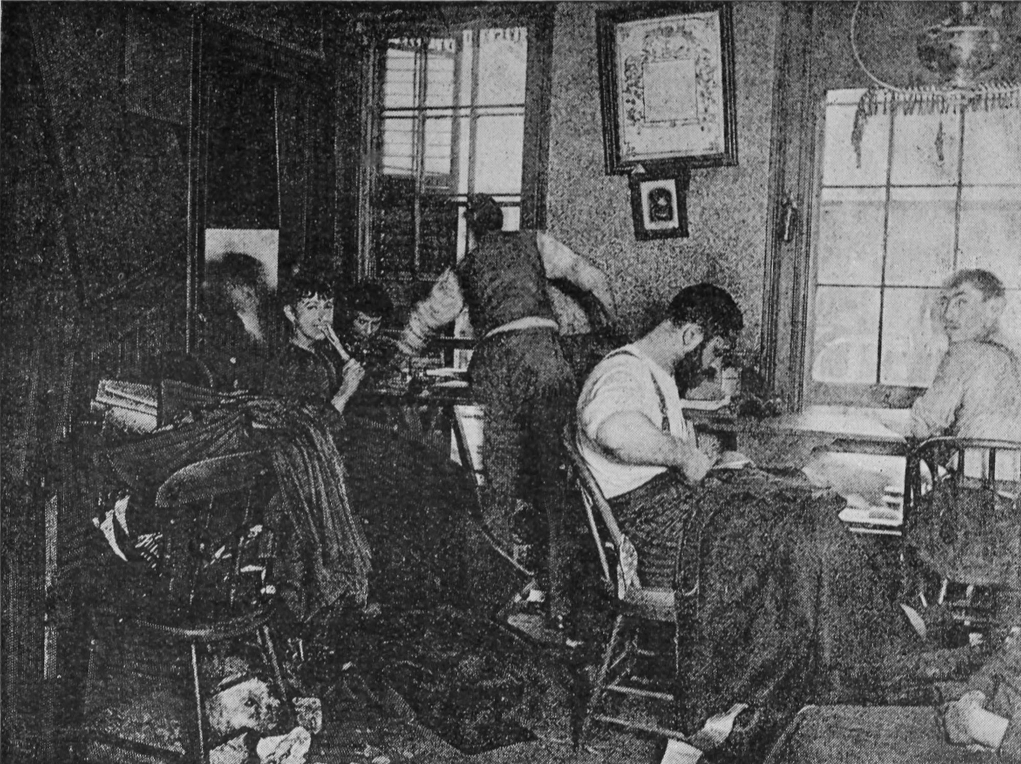 Several people sit in a room with piles of fabric, sewing.