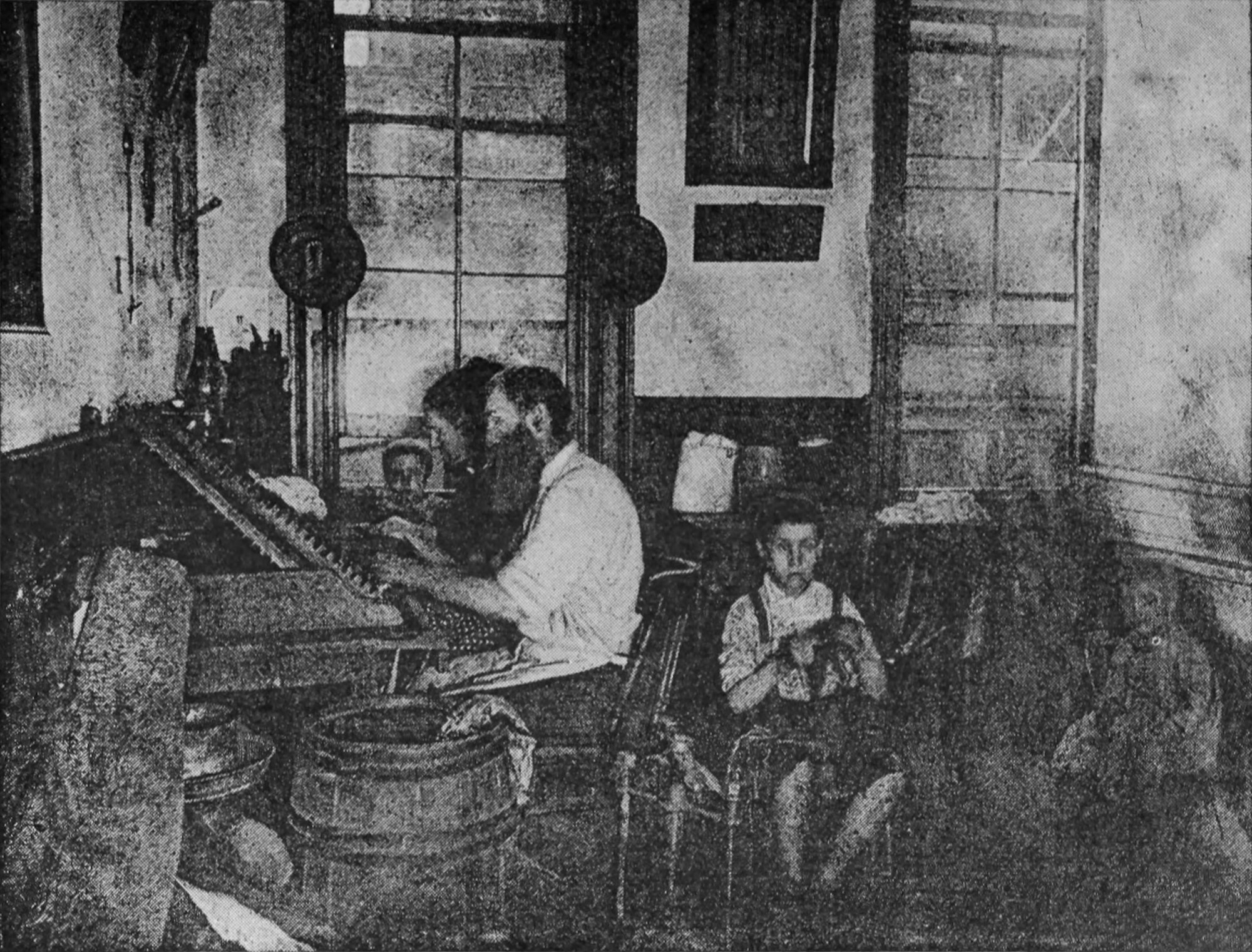 Some adults sit at a workstation, and some children are seated nearby.