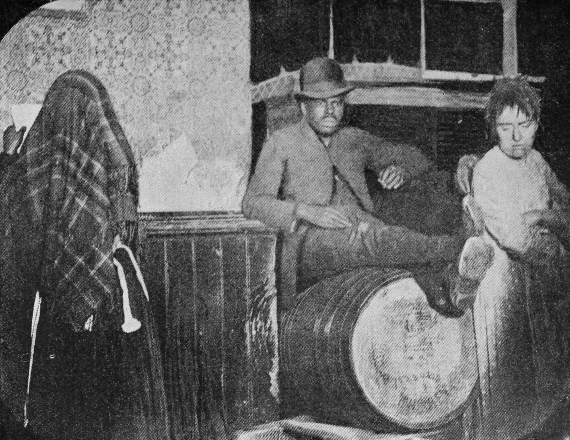 A man wearing a hat sits on a barrel, and two women are standing nearby.