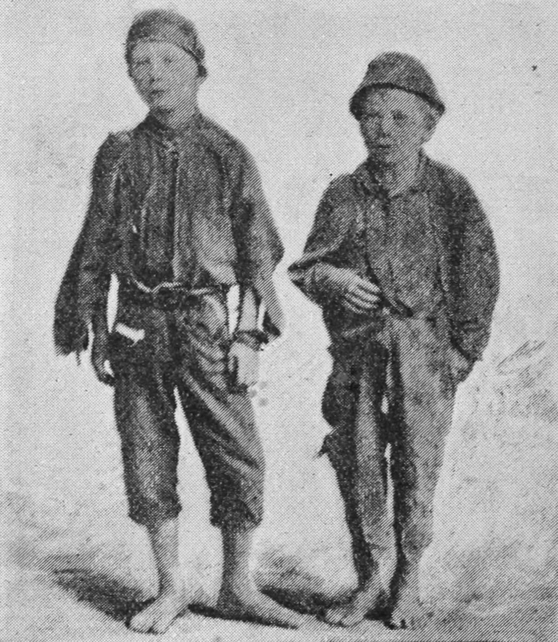 Two small boys in ragged clothing are barefoot.