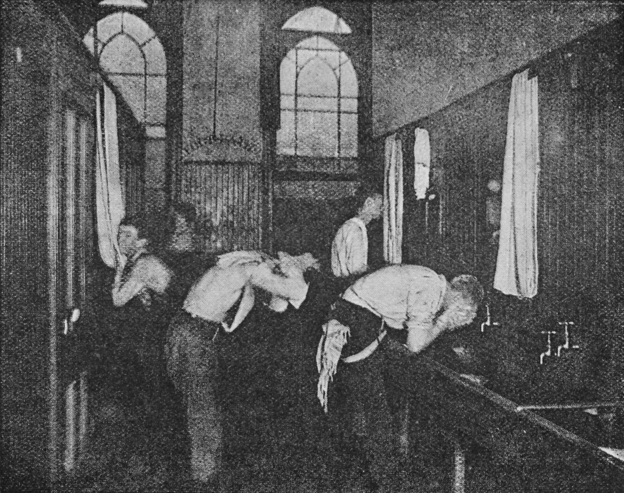 Boys are washing themselves in front of a row of sinks.