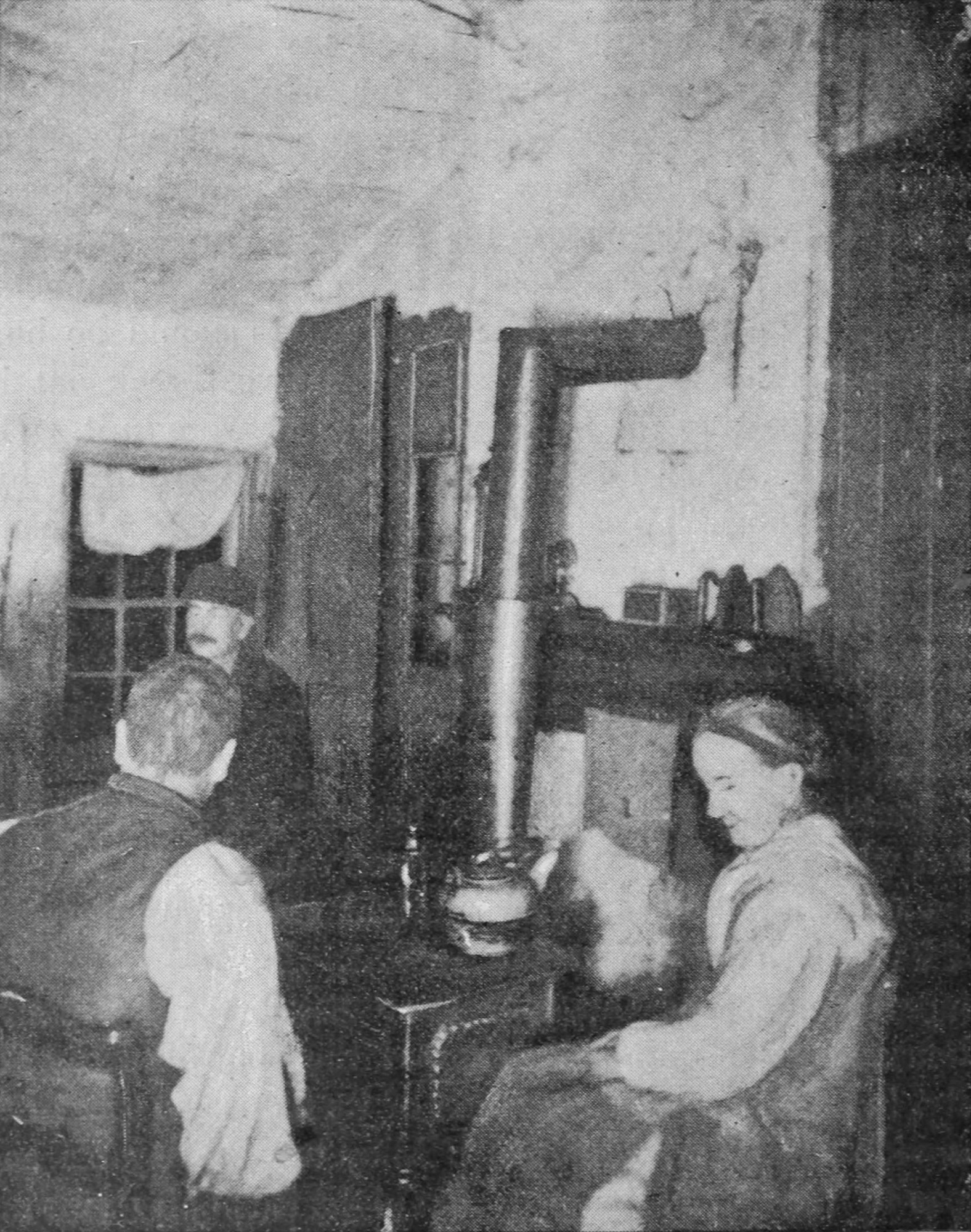 Two men and a woman sit around a stove.