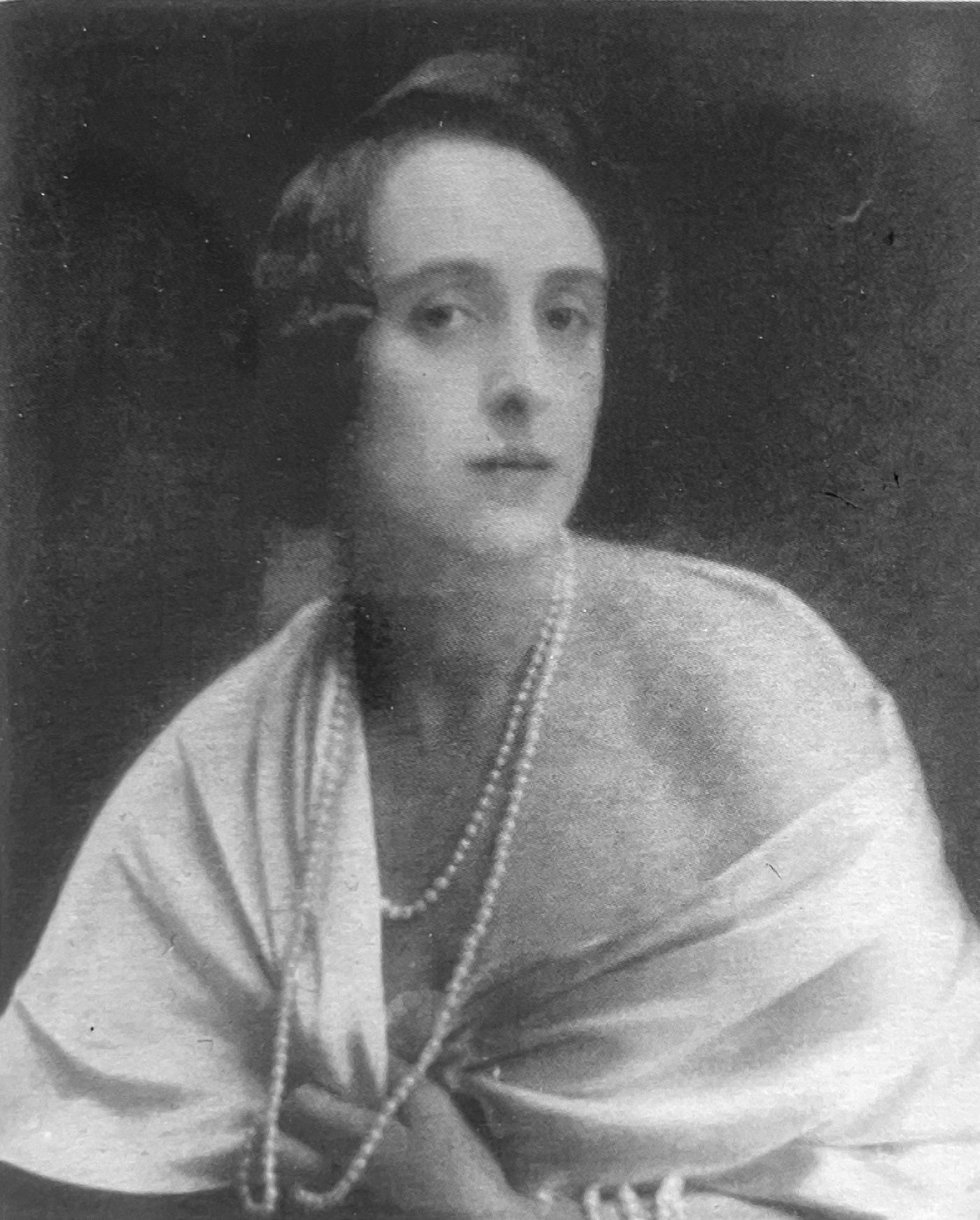 A young woman with shorter hair wearing pearls and white robes that leave one shoulder bare.