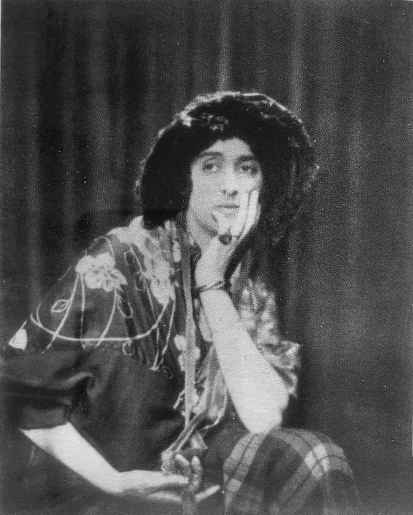 A woman wearing a bonnet sits with her head in a hand and elbow resting on her knee.