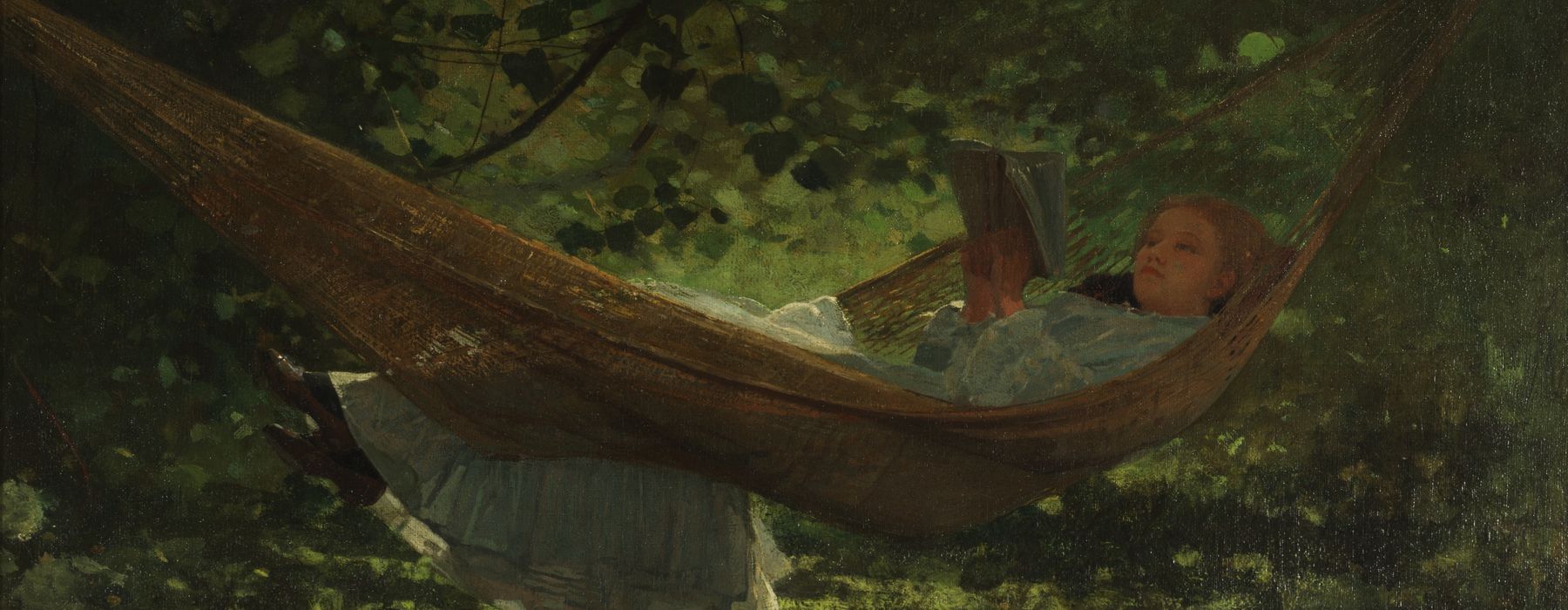 A girl reclines in a hammock and reads a book.